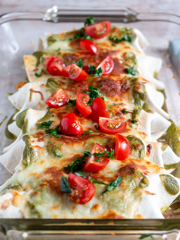 Burritos topped with chopped tomatoes and cilantro in a clear 9 x 13 baking dish.