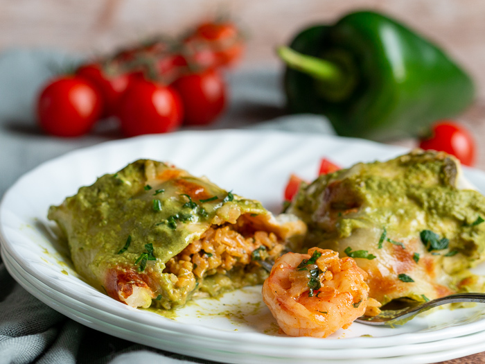 Shrimp Burritos with Creamy Poblano Sauce cut in half to show the shrimp and rice mixture on a white plate.