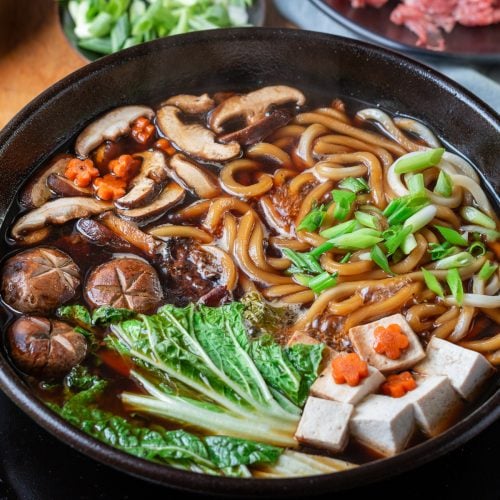 Sukiyaki Beef Udon cooking with tofu, mushroom noodles and vegetables in a black pot.