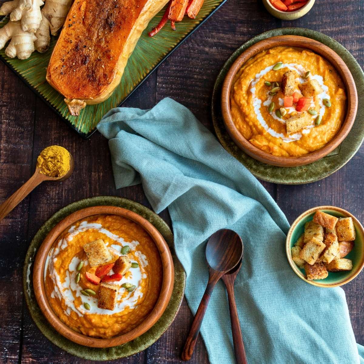 2 bowls of cozy autumn soup with a half of roasted winter squash and a side of croutons.