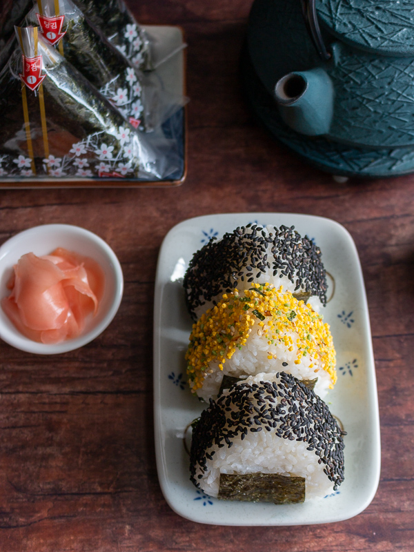 Top down photo of 3 onigiri with 2 with black sesame sprinkles and one with tomago (egg) sprinkles on top. 