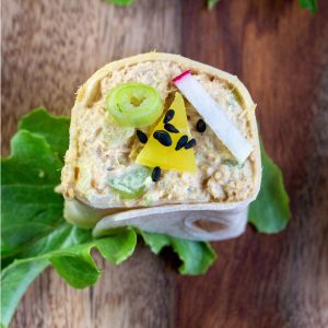 Delicious roll up sandwich garnished with Japanese pickles and radishes and green onions on a wooden board.