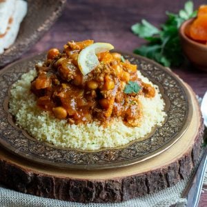 Moroccan Lamb Stew on a bed of couscous on a gold plate on top of a wooden board and garnish with lemon.