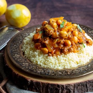 Delicious plate of lamb Moroccan stew on a gold plate elevated up on a wooden board with lemons in the background.