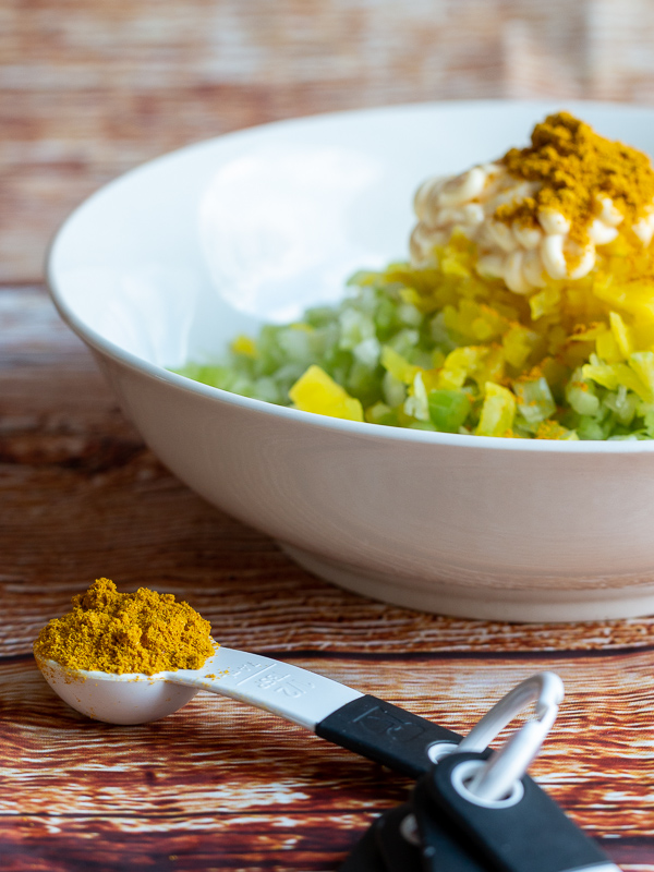 Heaping teaspoon of mild yeloow curry next to a bowl of tuna salad ready to be mixed. 