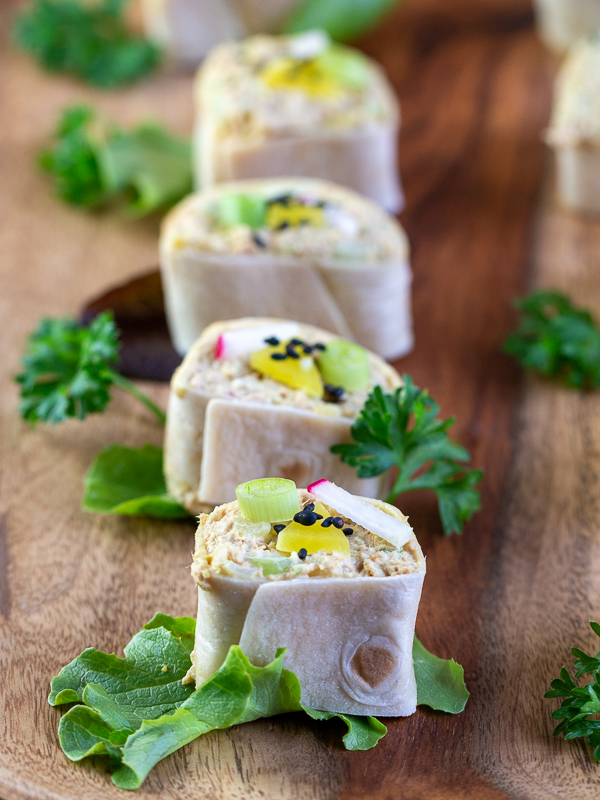 4 tuna rolls all decorated with garnishes on a wooden plate.