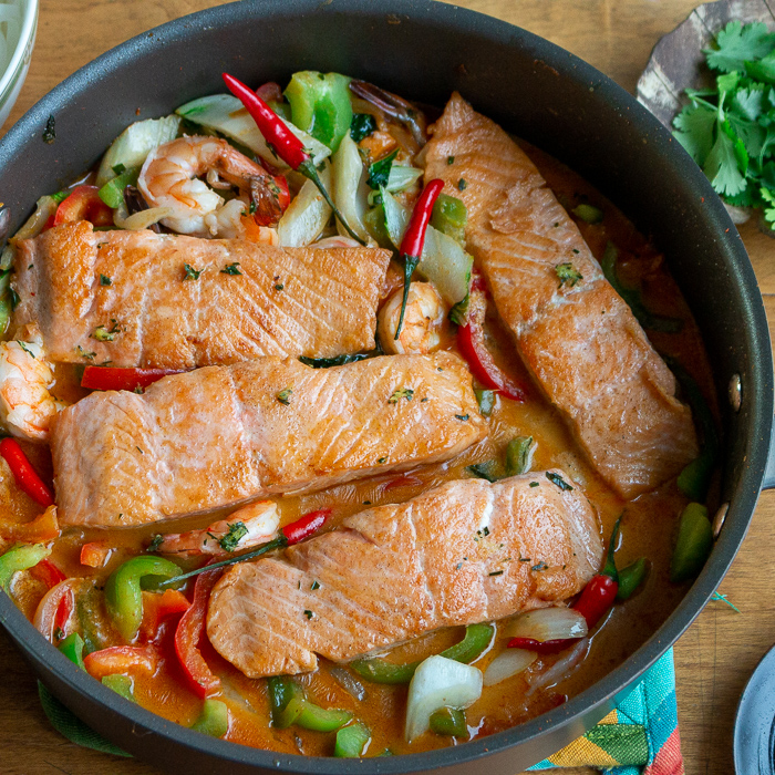 4 salmon fillets in a spicy Thai curry broth with vegetables in a black pan. 