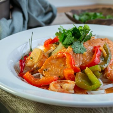 Salmon curry in a white bowl with a coconut sauce and vegetables garnished with fresh cilantro.