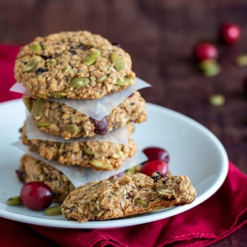 Cranberry Oatmeal Breakfast cookies stack with 4 on a white plate with one of them with a big bite out of it.