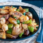 Piled in a black bowl is roasted crispy potatoes, green peppers, onions and shrimp.