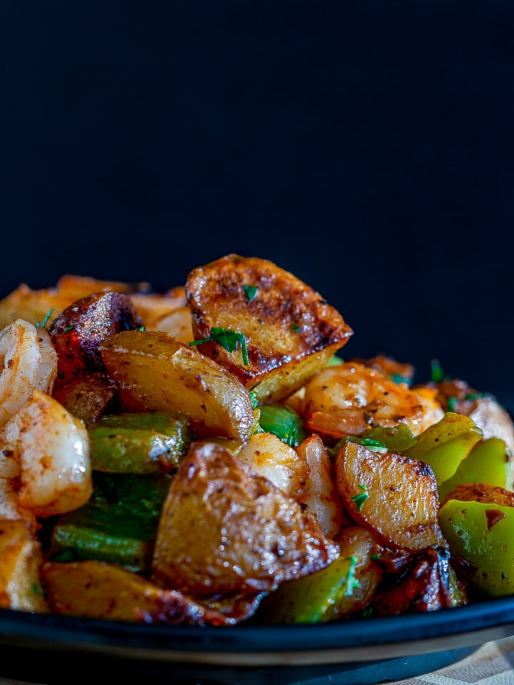 Piled in a black bowl is roasted crispy potatoes, green peppers, onions and shrimp.