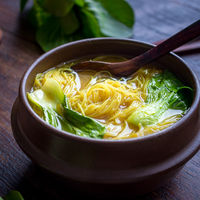 Golden Spiced Noodle Soup with bok choy in a  brown soup bowl with soup spoon.