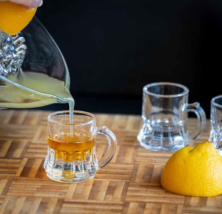 Lemon juice getting poured into the whiskey and honey in the shot glass.