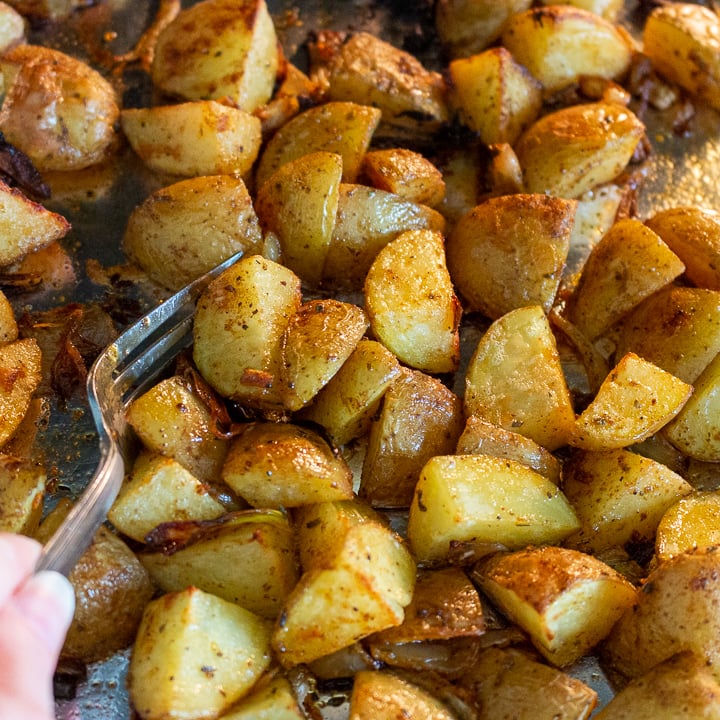 Potatoes getting tossed on the sheet pan part way through the roasting process.