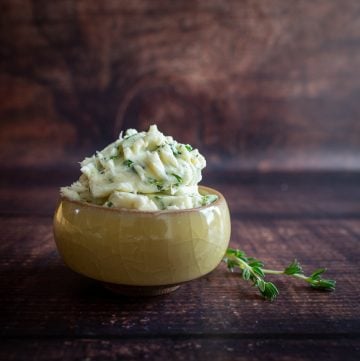Whipped herb butter in a small yellow bowl with a sprig of thyme.