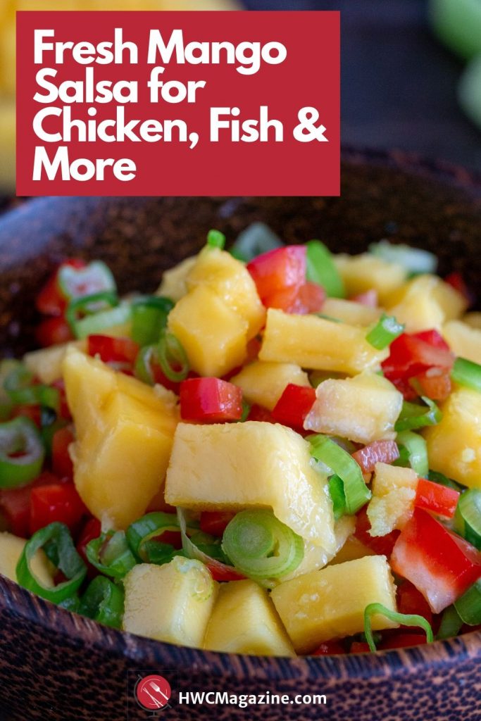 Wooden bowl of delicious fresh mango salsa with a half a a mango slice and green onion on the side.