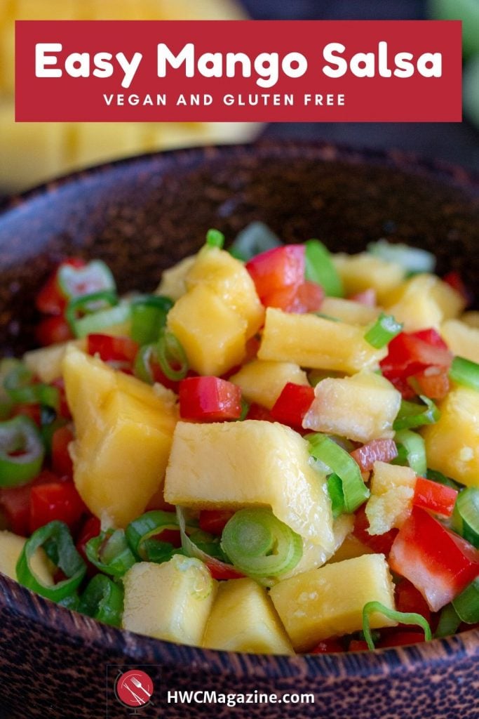 Wooden bowl of delicious fresh mango salsa with a half a a mango slice and green onion on the side.