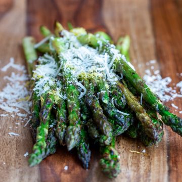 Grilled asparagus on a wooden board with lemon and parmesan.
