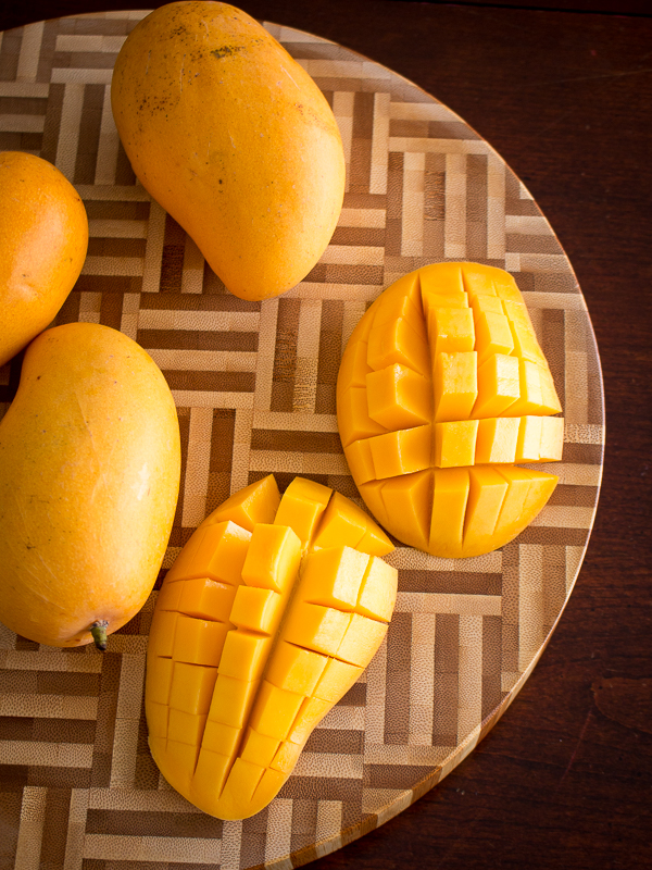 Mangoes slices and checkerboard sliced on a wooden cutting board. 