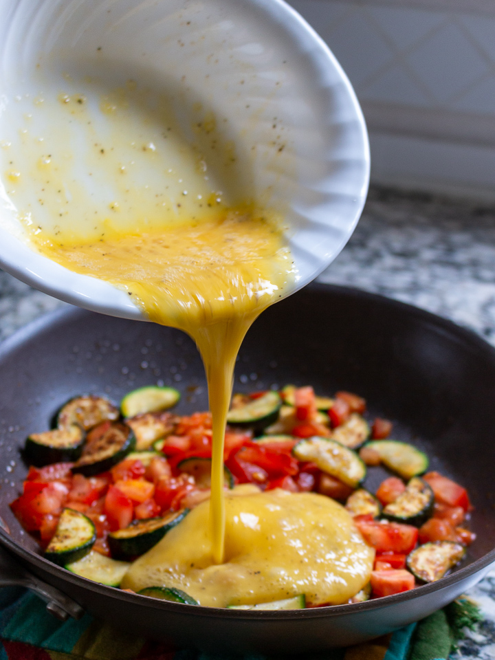 Beaten Eggs getting poured into a pan with the cooking vegetables.