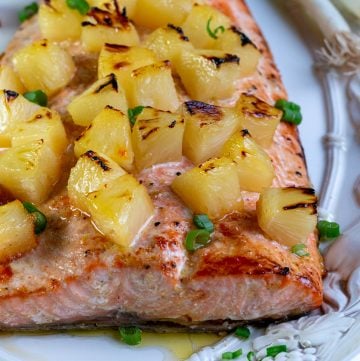 Baked whole salmon with toasty pineapple chunks on a white plate, garnished with green onions.
