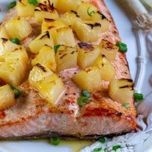 Baked whole salmon with toasty pineapple chunks on a white plate, garnished with green onions.
