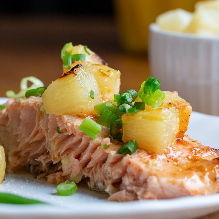 Pineapple Glazed Salmon served on a white plate with a side of green beans and extra cup of pineapple in the background.