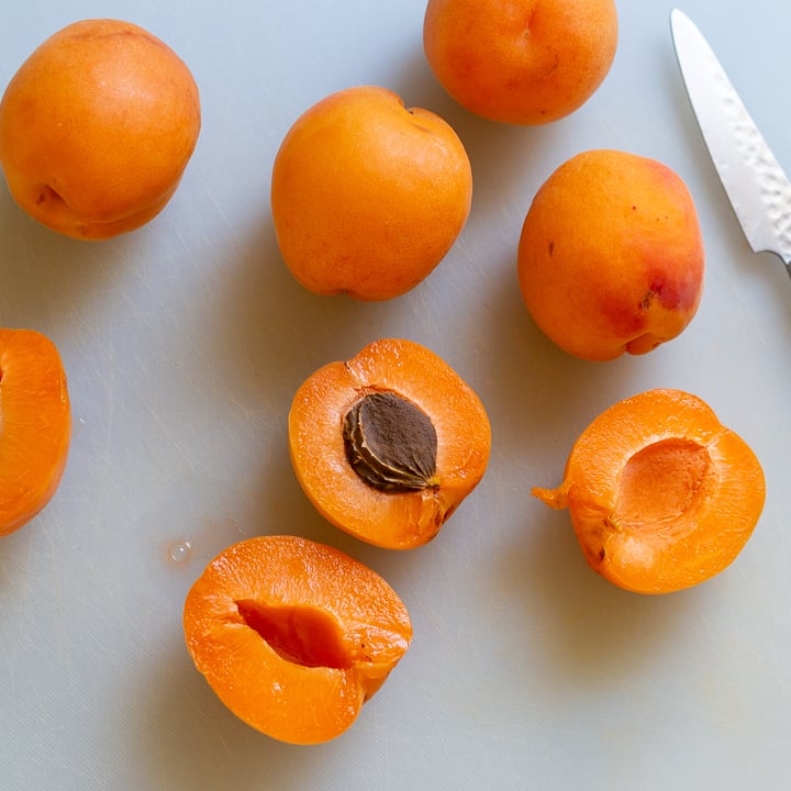Fresh apricots on a white cutting board cut in half.