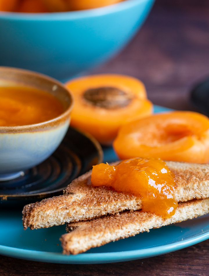 2 slices of toast with apricot freezer jam and fresh apricots on a blue plate.