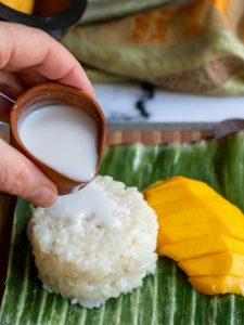 Coconut cream getting poured over sticky rice.