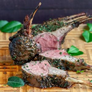 Whole Herb Marinated Grilled Rack of Lamb cut into slices on a cutting board with fresh herbs.