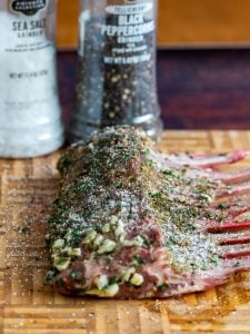 Marinated leg of lamb getting salted and pepper just before placing it on the grill.