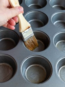 Brushing the cupcake pan with butter.