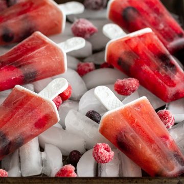 Rainbow Berry Rooibos Ice Pops on a sheet pan with ice and frozen mixed berries.