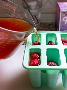 Rainbow Rooibos Tea getting poured over the frozen berries in the popsicles molds.