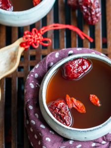 Delicious cup of Goji Berry and Red Dates Herbal tea in white tea cup garnished with extra dates on a Chinese Tea table.