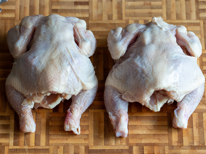 2 uncooked Cornish Game Hens on a cutting board. 