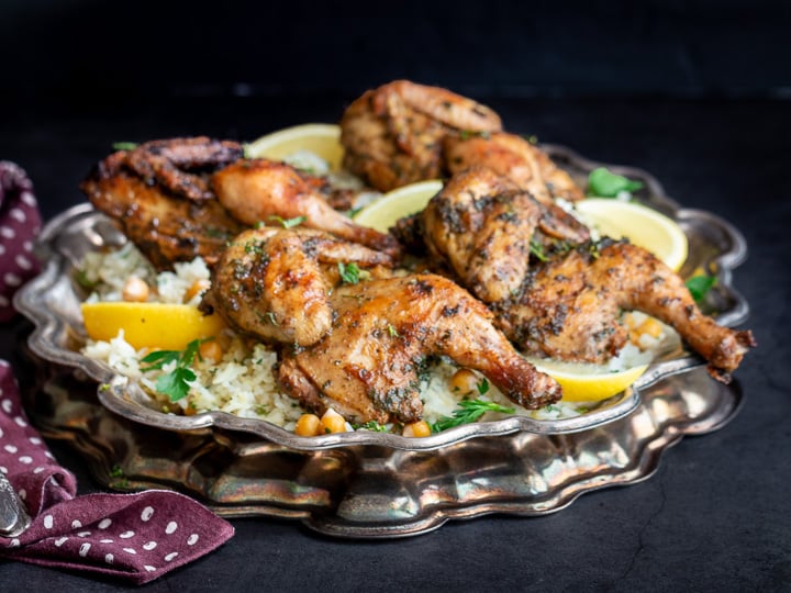 Dinner is served with a delicious plate of 4 perfectly grilled split Cornish game hens on a platter of lemon rice on a platter.
