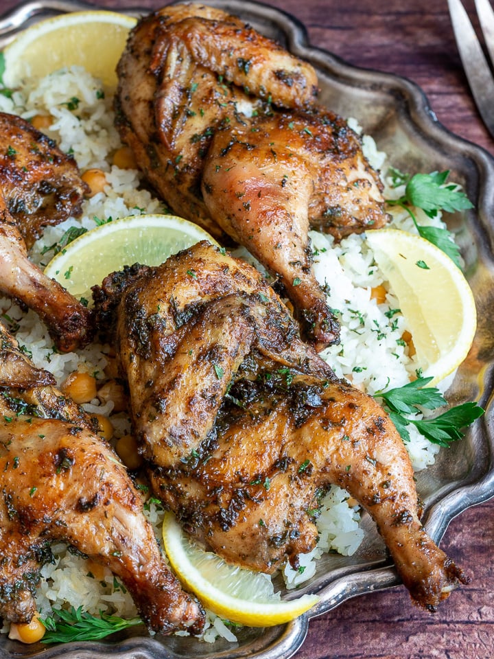 Close up shot of 4 little split Cornish hens on plate garnished with parsley and lemon slices. 