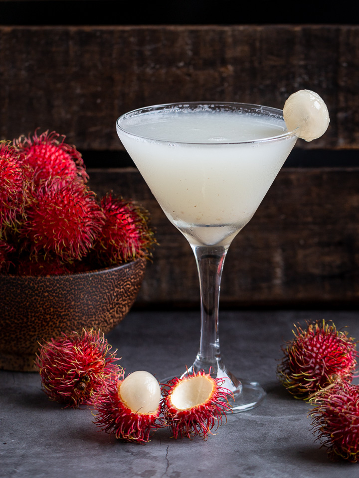 Snow flaky cold Rambutan Cocktail in a martini glass with a bowl of fresh rambutans in a wooden bowl.