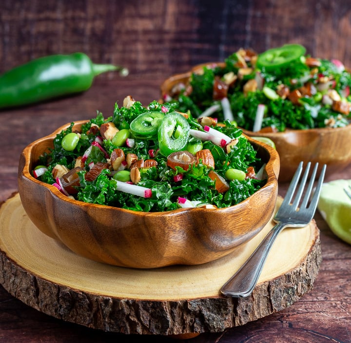 Two delicious bowls of Autumn kale salad in wooden bowls tossed with almonds and dates. 