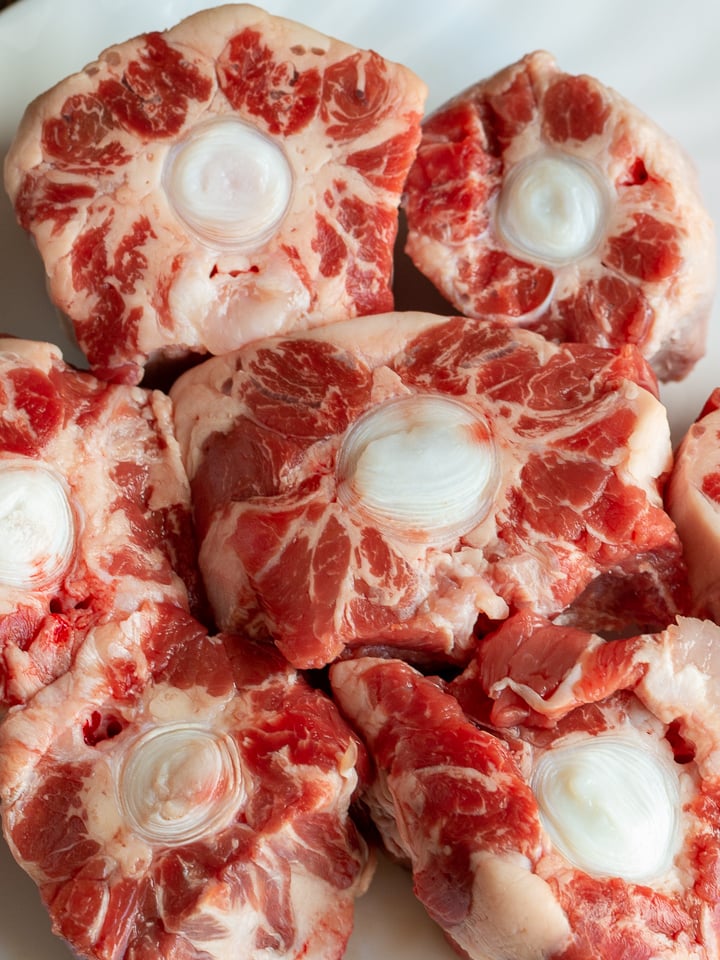 Uncooked beef oxtail on a white plate.