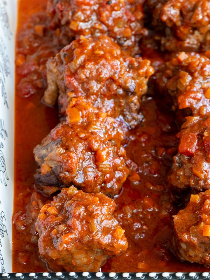 Cooked osso buco in a black and white dish with lots of red wine tomato sauce.