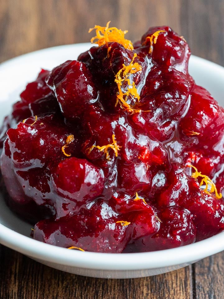 Honey sweetened cranberry sauce in a white bowl topped with orange zest.
