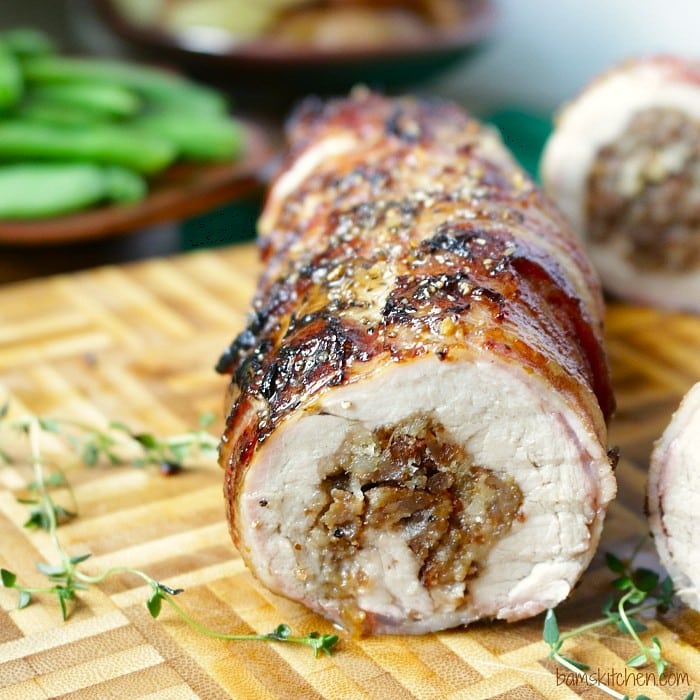 Grilled Bacon wrapped pork tenderloin stuffed with sausage sliced open to show the juicy meat on a cutting board.