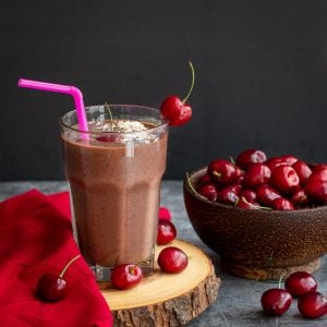 Mexican chocolate cherry smoothie on a wooden serving platter garnished with cherries.