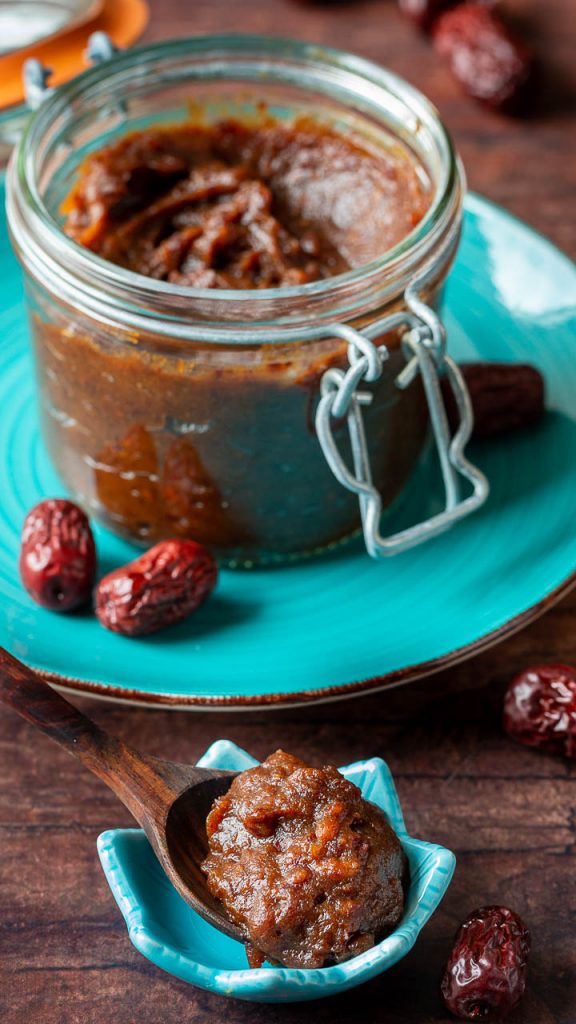 Dollop of red date paste on a wooden spoon.