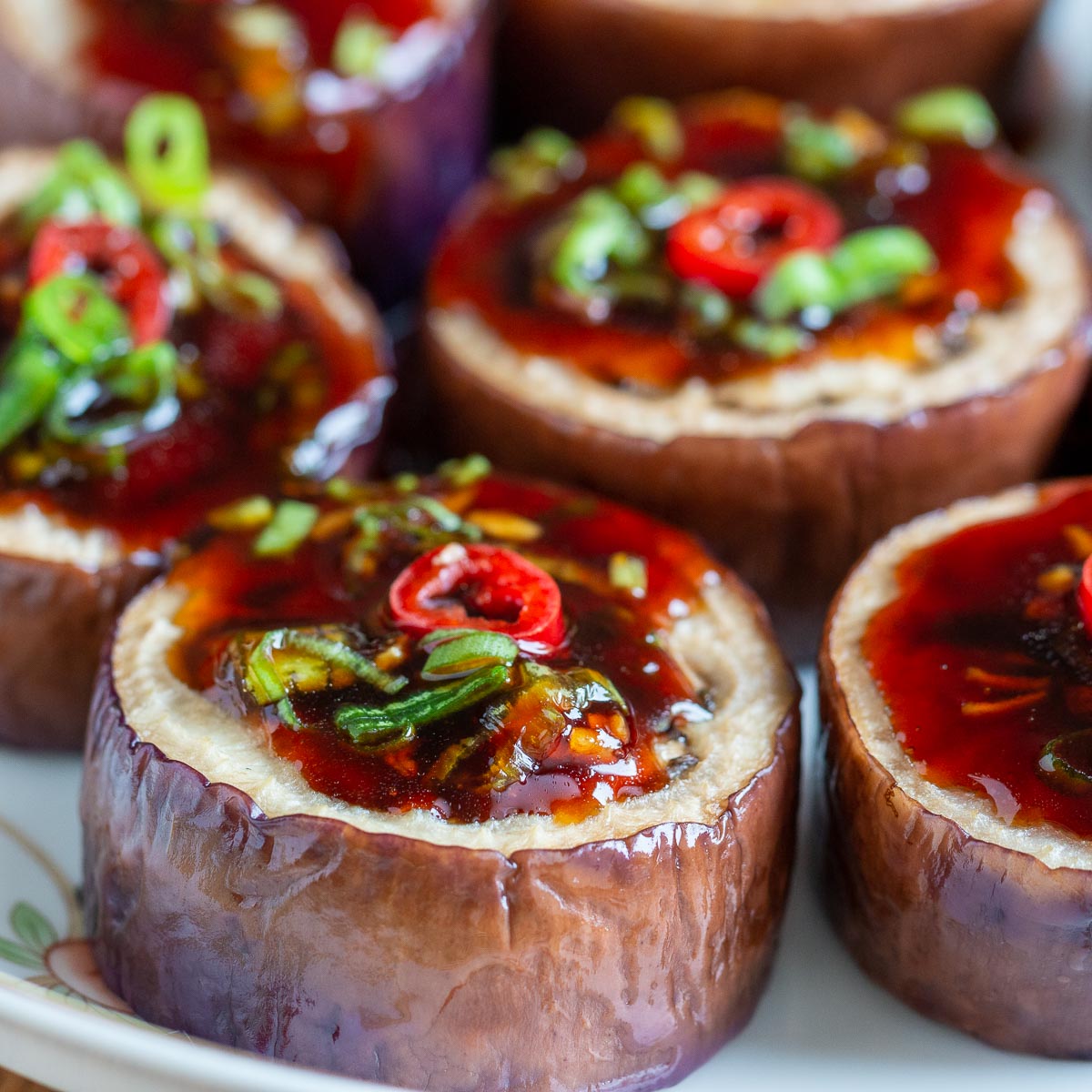 Air fried eggplant with garlic sauce topped with green onions and chilis on white plate.