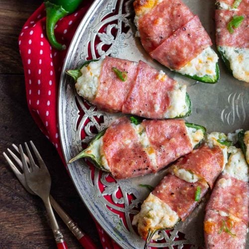 Air fryer jalapeno poppers on a silver platter wrapped in salami.