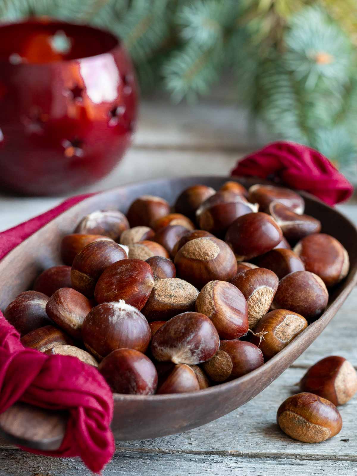 Raw chestnuts in a wooden bowl with holiday decorations around the bowl.